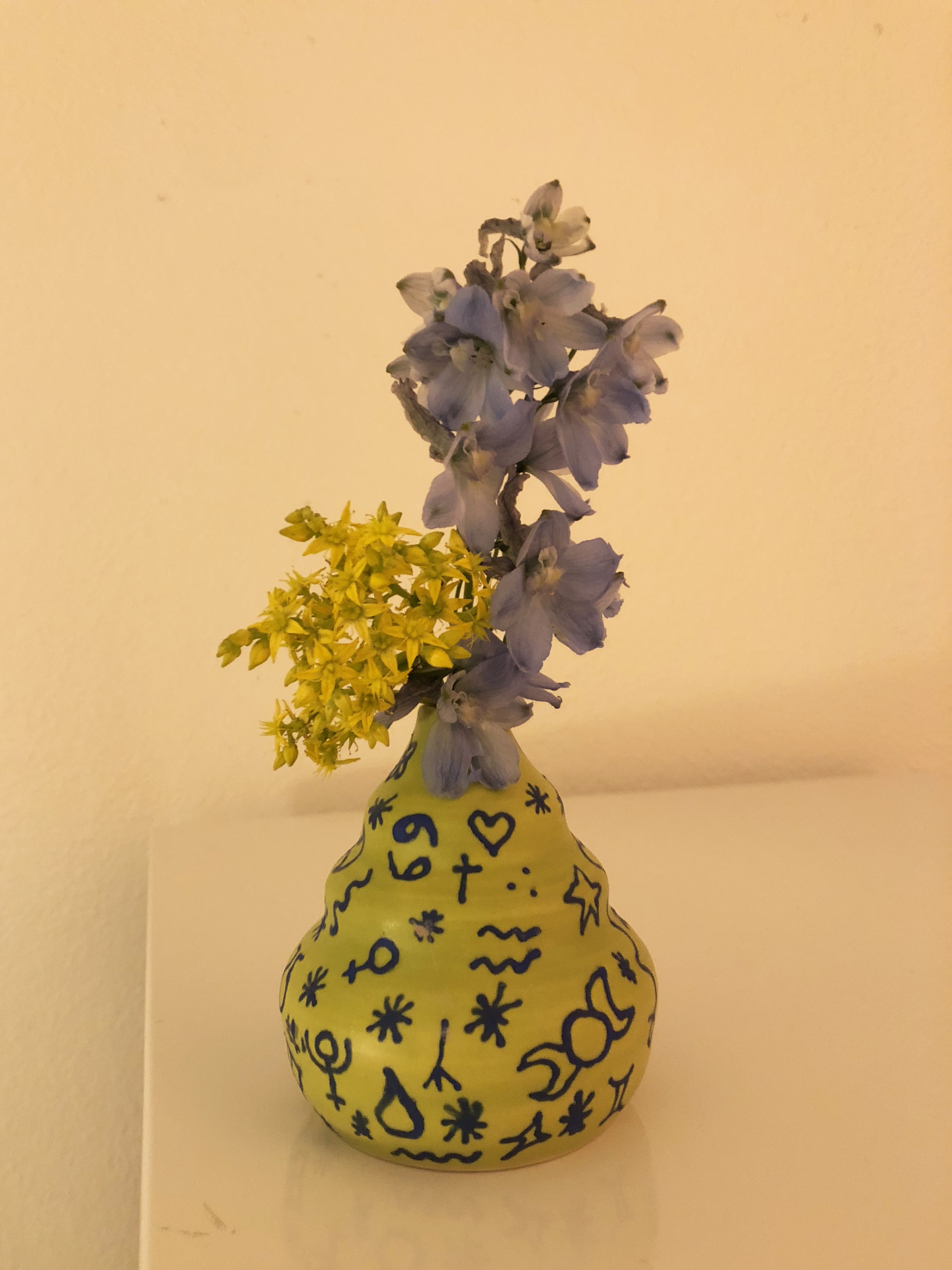 A ceramic green vase covered in drawings with blue and yellow flowers in it